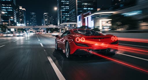Red luxury car accelerating away at night with glowing taillight streaks